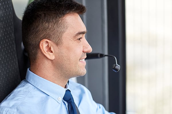 Side view of an attractive 30-something ethnic man with dark, short hair, thick eyebrows, wearing a blue button-down dress shirt with a darker blue tie, bus driver with an installed microphone