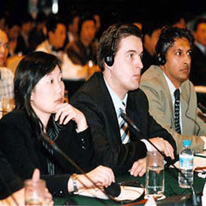 People of different nationalities sitting wearing headsets listening to someone speak at a conference center