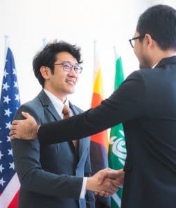 Business man shaking hands with a man in front of international flags.